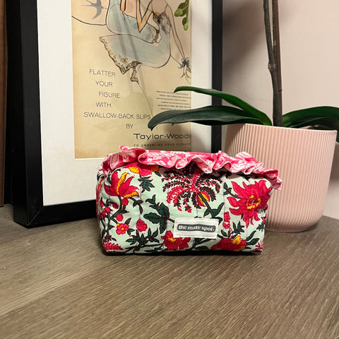 Floral-patterned pouch on a wooden surface with a framed picture in the background made at TMS