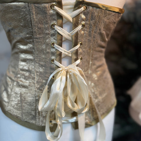 Close-up of a metallic corset with white laces on a blurred background