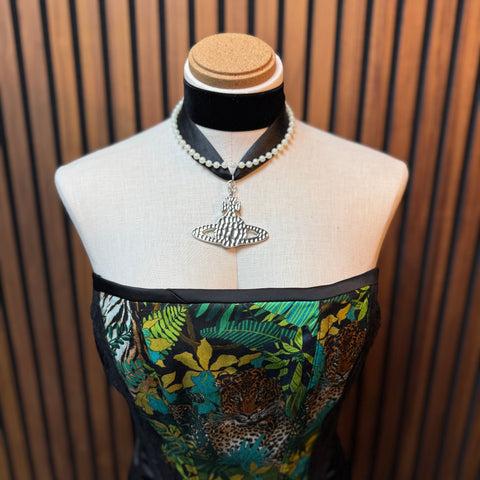 Mannequin wearing a patterned dress with a necklace and pendant against a wooden paneled background