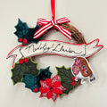 Decorative Christmas ornament with holly leaves, berries, and a red ribbon on a white background. made at TMS