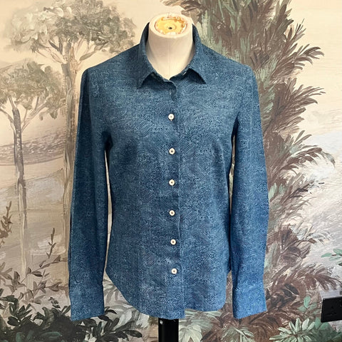 Blue shirt on a mannequin against a decorative wall with nature-themed wallpaper made at TMS